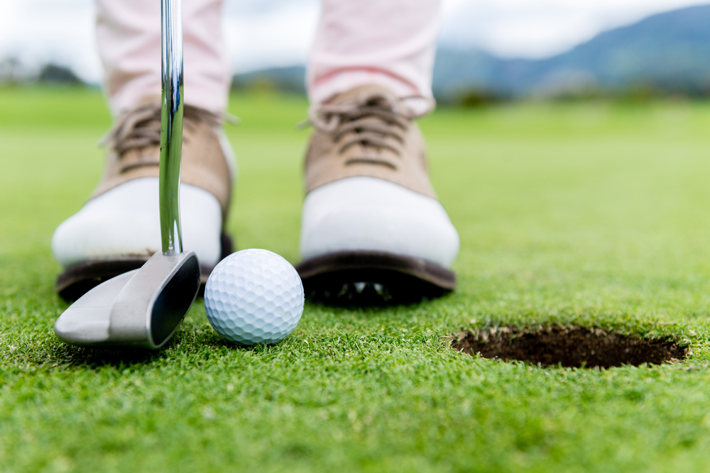 Golf player at the putting green hitting ball into a hole Golf player at the putting green hitting ball into a hole