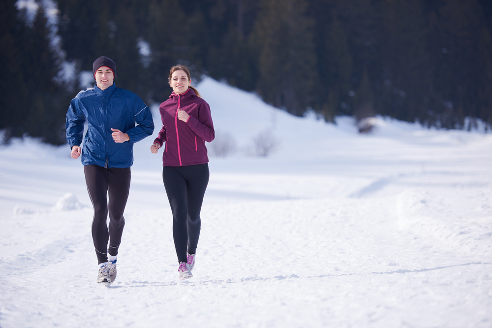 healthy young couple jogging outside on snow in forest. athlete running on beautiful sunny winter day healthy young couple jogging outside on snow in forest. athlete running on beautiful sunny winter day